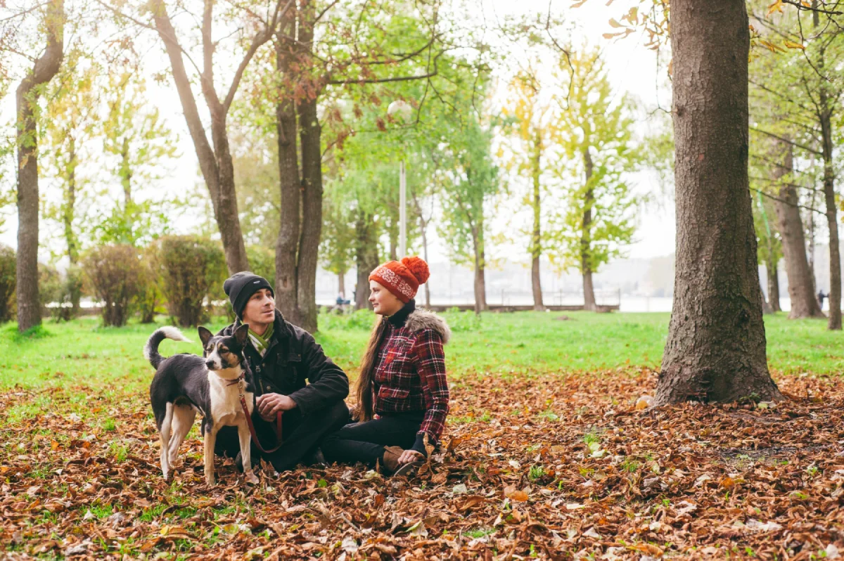 a man and a woman sitting in the leaves with a dog